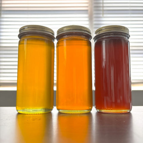 Three jars of honey with different colors on a reflective surface.