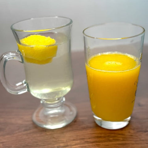 Two glasses on a wooden surface. One contains clear liquid with floating orange block. The other contains orange liquid.