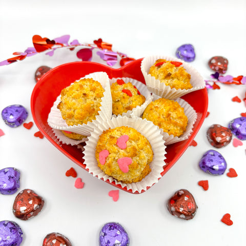 Honey macaroons in red, heart-shaped bowl surrounded by purple and red decorations on white background