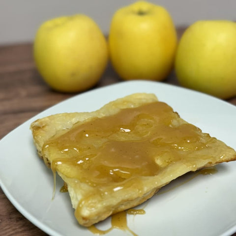 Honey apple puff pastry and caramel sauce served on a white plate with yellow apples in background.