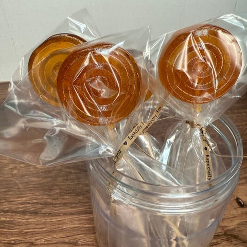 Wrapped honey lollipops in a clear jar on a wooden surface