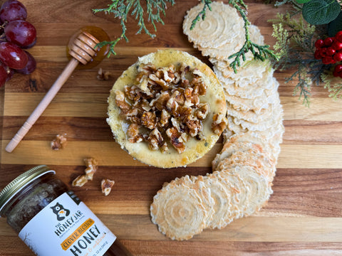 Cheesecake topped with nuts and surrounded with crackers, a jar of honey, and a honey dipper, all on a wooden surface.