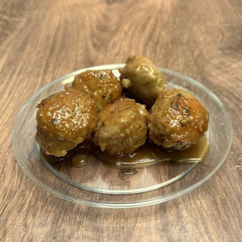 Meatballs on a clear plate sitting on a wooden surface