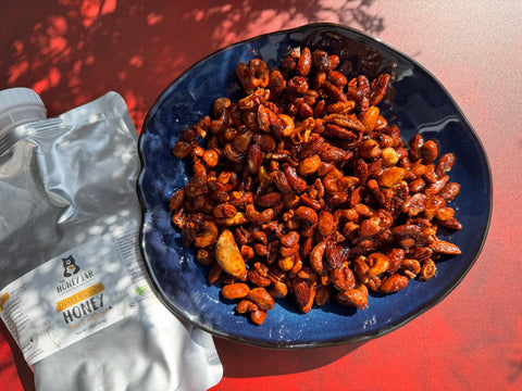 Mixed nuts in blue bowl next to container of honey on a red background