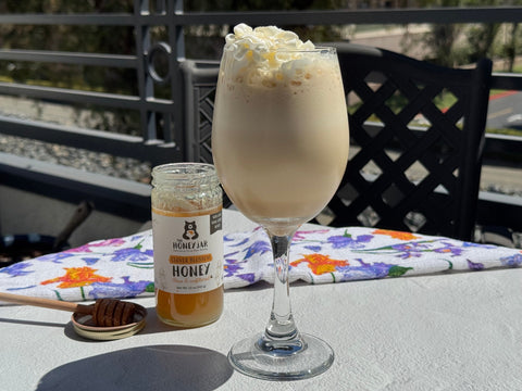 Glass of frappuccino on white table with jar of honey and patterned fabric behind