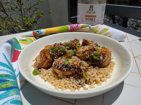 Shrimp and rice in a white bowl on a patterned background with a jar of honey in the background