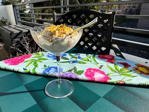 Glass filled with yogurt and topped with nuts and a spoon on patterned surface