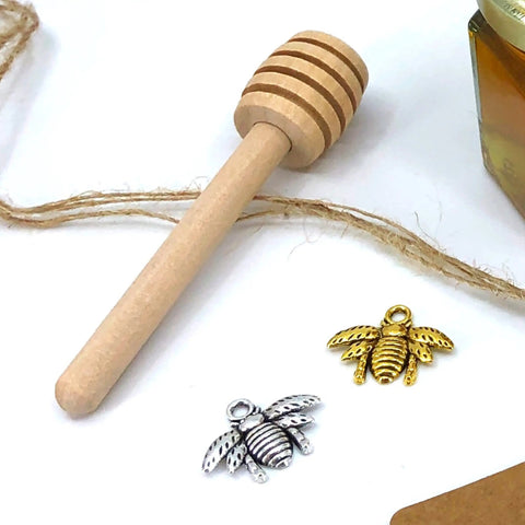 Honey dipper, bee charms, and twine scattered on white surface