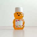 A small bear-shaped honey bottle filled with amber honey, featuring a white screw cap and a personalized white label with colorful fruit illustrations, 'Shana Tovah', and 'Jonah & Rachel'.