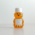 A small bear-shaped clear plastic bottle filled with amber honey, with a white screw cap and a custom printed label reading 'Shana Tovah' and 'The Stewart Family' on a white surface against a light background.