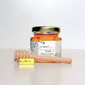 Jar of honey with a decorative label and wooden honey dipper on a white background