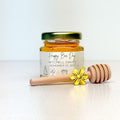 jar of honey with gold lid, label, wooden honey dipper, and gold flower charm on neutral background