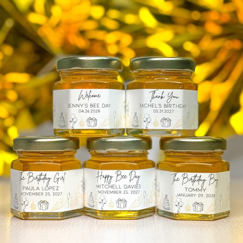 Five jars of honey with personalized labels on a wooden surface with a blurred golden background.