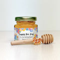 Honey jar with colorful label, wooden honey dipper, and honeycomb charm on a white background