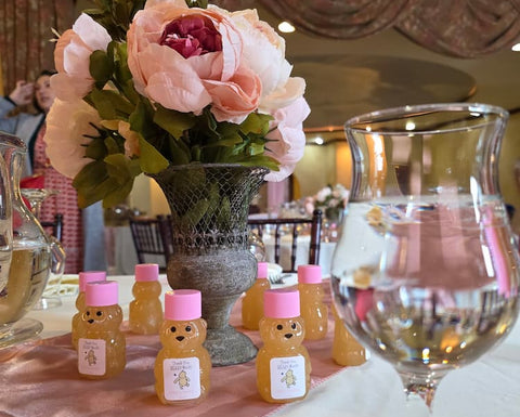 Decorative setup with small bear-shaped bottles, pink caps, and a floral arrangement on a table.
