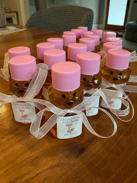 Honey bears with pink tops, white ribbon, and personalized labels on a wooden table.
