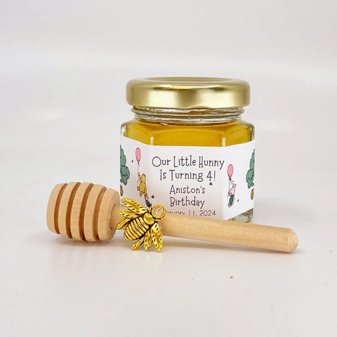 2 oz hexagon jar filled with honey, gold lid, gold bee charm, 3" wooden honey dipper and personalized Winnie the Pooh design on label with pink balloons and Our Little Hunny is Turning 4 title.