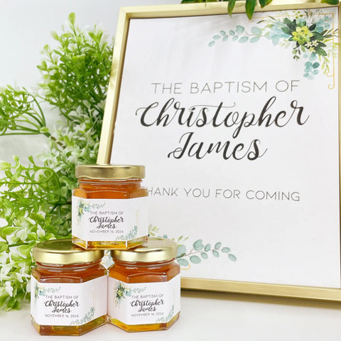 2 oz baptism favors on hexagon jars with gold lid and personalized labels. Labels feature gold frame with eucalyptus leaves with The Baptism of Christopher James as a title. Matching printable table sign in background.