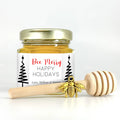 2 oz hexagon honey favor. Jar is filled with honey and has gold lid, 3" wooden honey dipper, gold bee charm, and personalized fine line trees label with title Bee Merry.