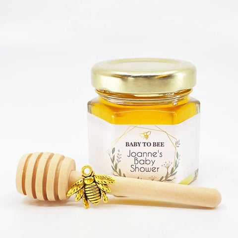 2 oz hexagon jar filled with honey, gold lid, 3" wooden honey dipper, gold bee charm, and personalized geometric design on label with title Baby to Bee.