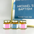 2 oz baptism favors on hexagon jars with gold lid and personalized labels. Labels feature a pink or blue graphics design. Matching printable table sign in background.