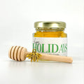 2 oz hexagon honey favor. Jar is filled with honey and has gold lid, 3" wooden honey dipper, gold bee charm, and personalized green holiday greeting design on label with title Happy Holidays.