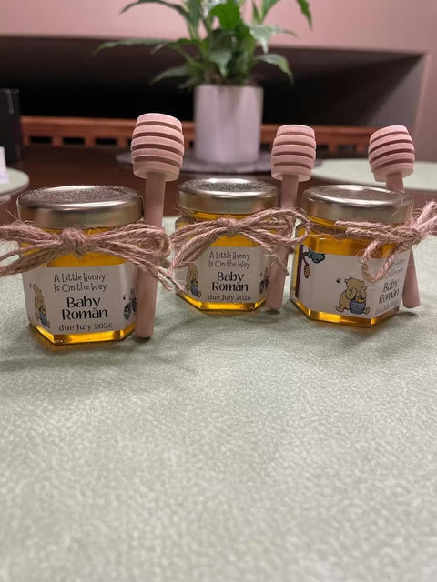 Four small jars of honey with personalized labels and honey sticks on a textured surface.