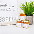 2 oz honey thank you wedding party shower favors on hexagon jars with gold lid with personalized labels. Labels feature black and white honeycomb design with Thank You title. Free matching printable table sign in background.