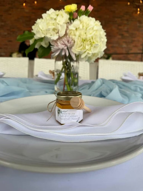 Small jar of honey on a white fabric with flowers in the background