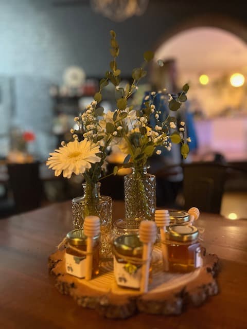 Floral centerpiece with jars of honey on a wooden surface.