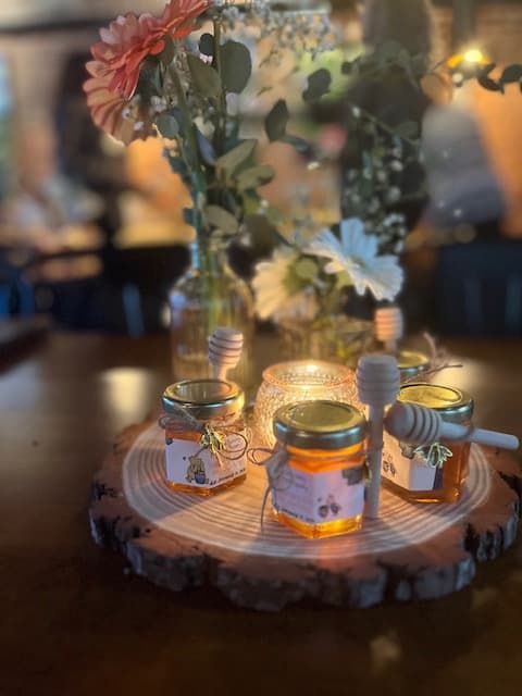 Three jars of honey on a wooden board with flowers in the background