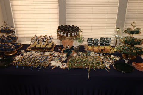 Table with various items including bottles of honey, a teddy bear, and cupcakes against a window with blinds.