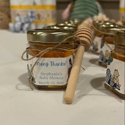 Jar of honey with a label for a baby shower, surrounded by similar jars on a table.