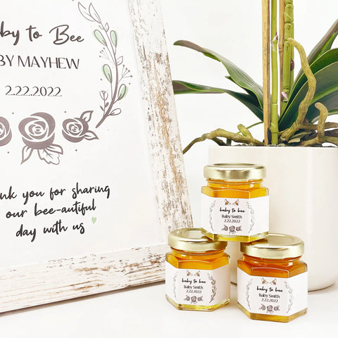 Rose laurel theme baby shower favors with personalized Baby to Bee label and gold lid. Free matching printable sign is in the background with title Baby to Bee.