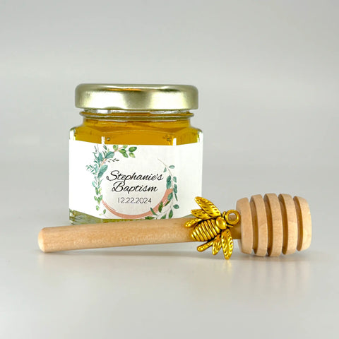 2 oz hexagon jar filled with honey, gold lid, 3" wooden honey dipper, gold bee charm, and personalized leaf frame design on label.