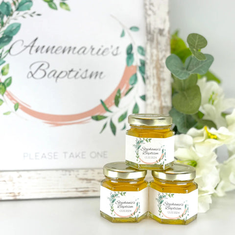 2 oz baptism favors on hexagon jars with gold lid and personalized labels. Labels feature a leaf frame design. Matching printable table sign in background.