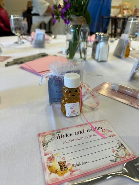 Table setting with a bottle of honey, small bag, and 'Advice and Wishes' card on a white tablecloth.