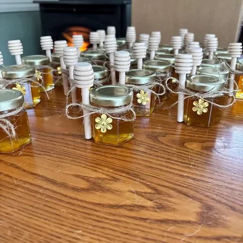 Jars of honey with honey dippers and flower charms on a wooden surface.