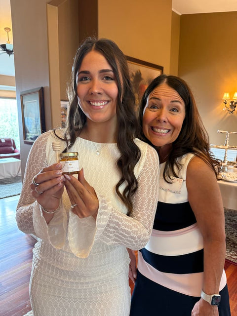 Two women standing in a room, one holding a jar of honey.