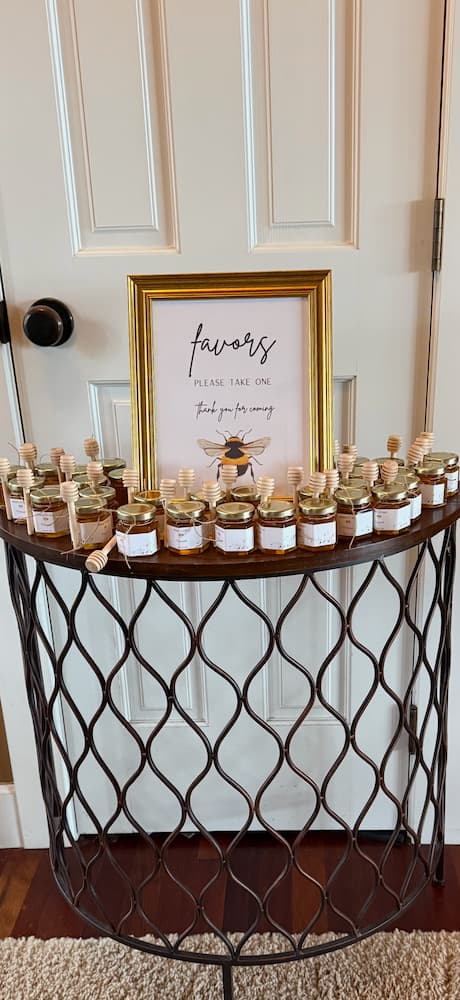 Table with small jars labeled 'favors' in front of a framed sign on a white wall.
