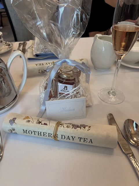 Gift bag with honey jar in front of sign with Mothers Day Tea on white tablecloth