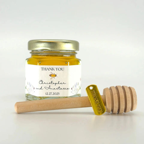 2 oz hexagon honey favor filled with honey. Jar has gold lid, 3" wooden honey dipper, gold Thank You charm, and personalized meadow design on label with title Thank You.