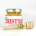 2 oz hexagon honey favor. Jar is filled with honey and has gold lid, 3" wooden honey dipper, gold bee charm, and personalized red holiday greeting design on label with title Merry Christmas.