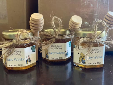 Three jars of honey with honey dippers and personalized labels on a reflective surface.