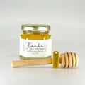 2 oz hexagon honey favor filled with honey. Also includes gold lid, 3" wooden honey dipper, gold Thank You charm, and personalized hand drawn floral design on label with title Thanks for Bee-ing Here.