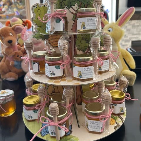 Three-tiered display of jars with Winnie the Pooh labels and honey dippers and a tree-themed stand on a table.