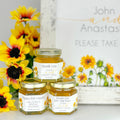 2 oz honey thank you wedding party shower favors with gold lid and personalized labels. Labels feature sunflowers and a variety of titles. Title shown include Thank You, Thanks for Bee-ing Here, and Thanks for Coming. Matching printable table sign in background.