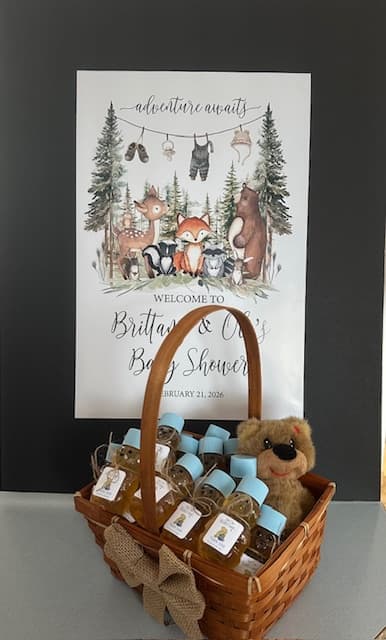 Baby shower basket with teddy bear and mini bottles of honey, in front of a baby shower sign.