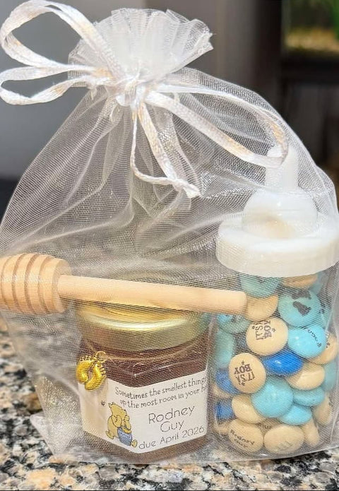 Gift bag with jar, honey dipper, and candy in a sheer bag on a countertop.