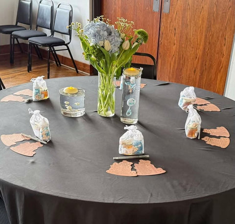 Decorated table with flowers, water glasses, and small bags on a gray tablecloth.